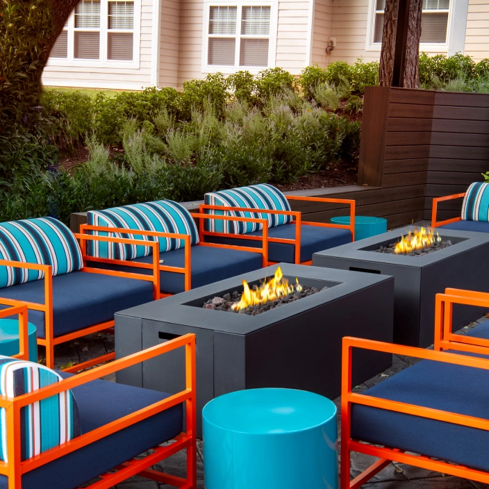 Colorful outdoor lounge chairs with striped cushions arranged around modern rectangular fire pits