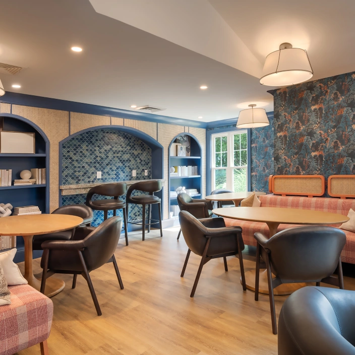 Inviting shared space with eclectic seating, patterned wallpaper, and arched bookshelf in background