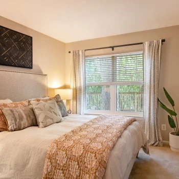 Bright bedroom with large window, patterned bedding, greenery, and modern framed wall artwork
