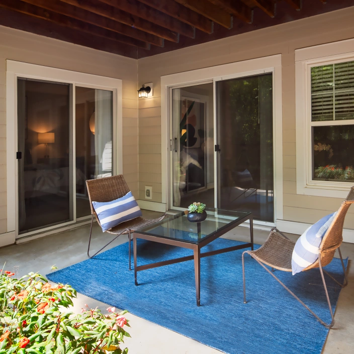 Outdoor patio with modern chairs, glass table, blue rug, and sliding glass doors