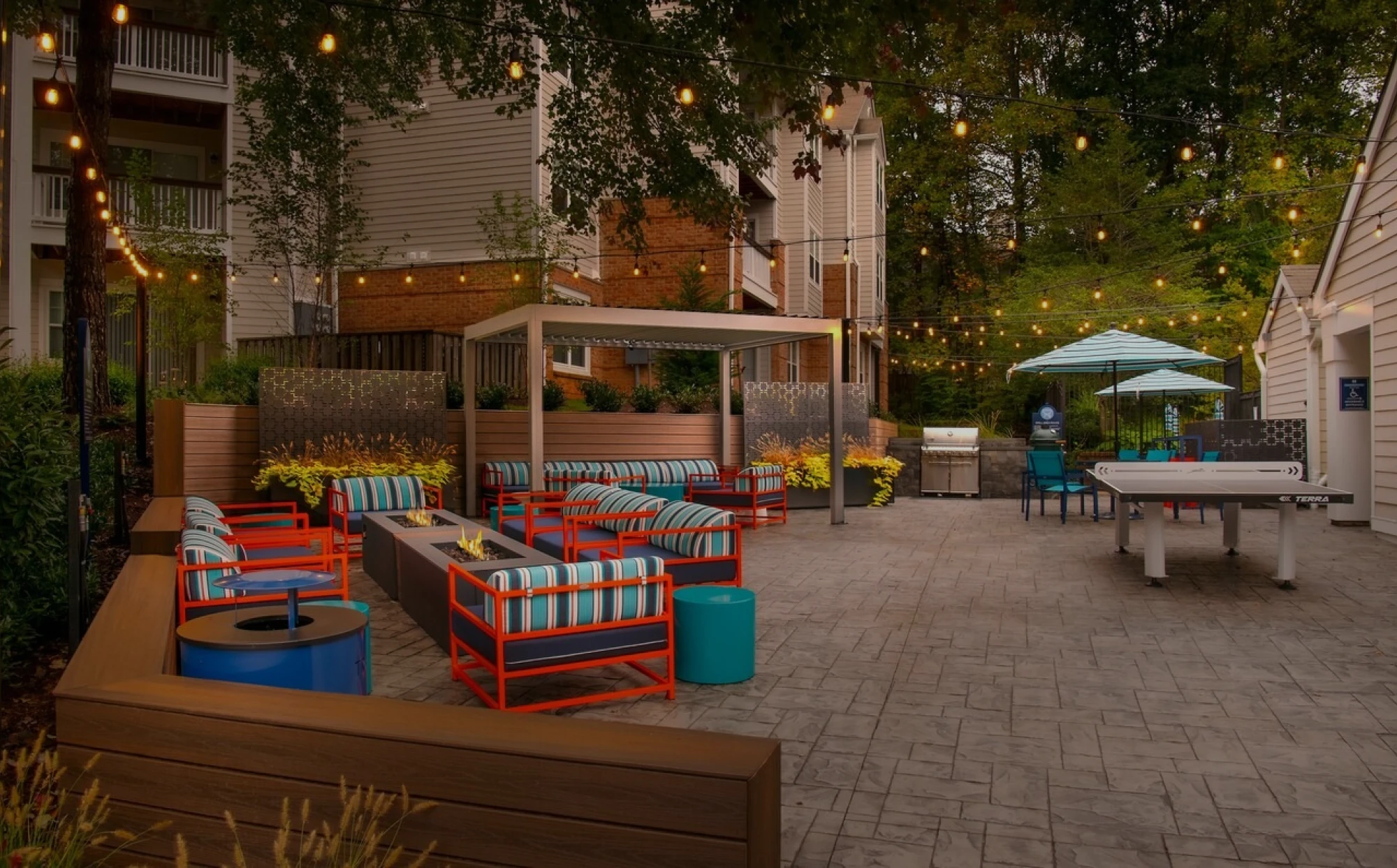 Outdoor lounge space with string lights, fire pits, and colorful seating at apartment complex