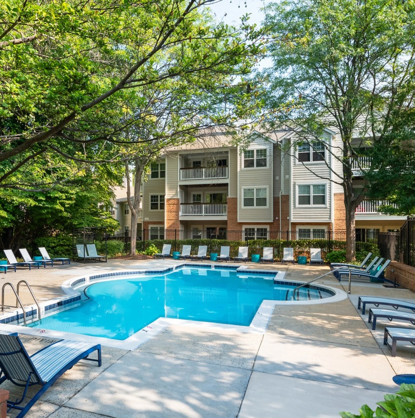Bright blue outdoor pool with sundeck seating nestled among apartment buildings and greenery