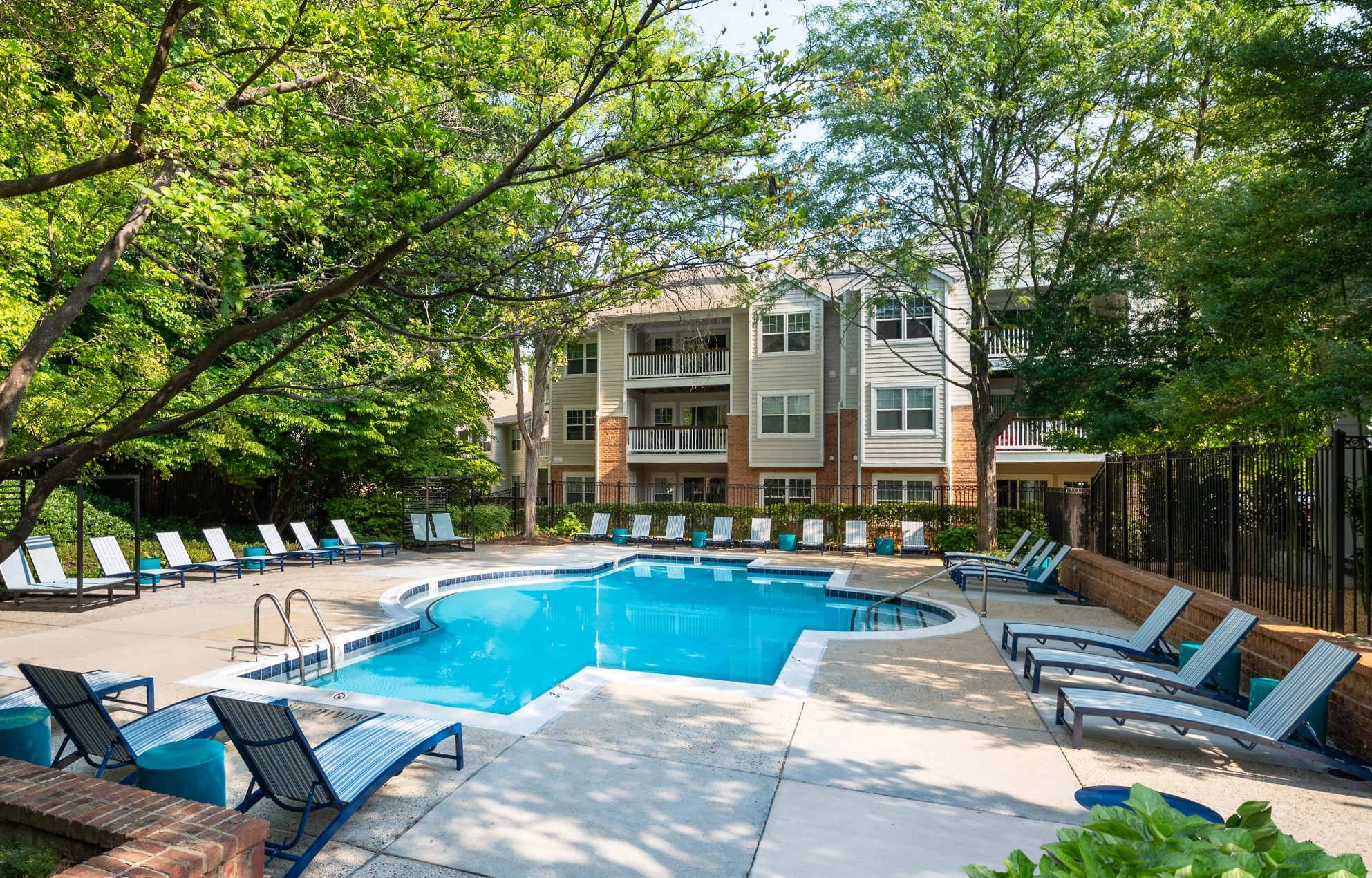 Resort-style pool area featuring modern lounge chairs, landscaped greenery, and spacious deck