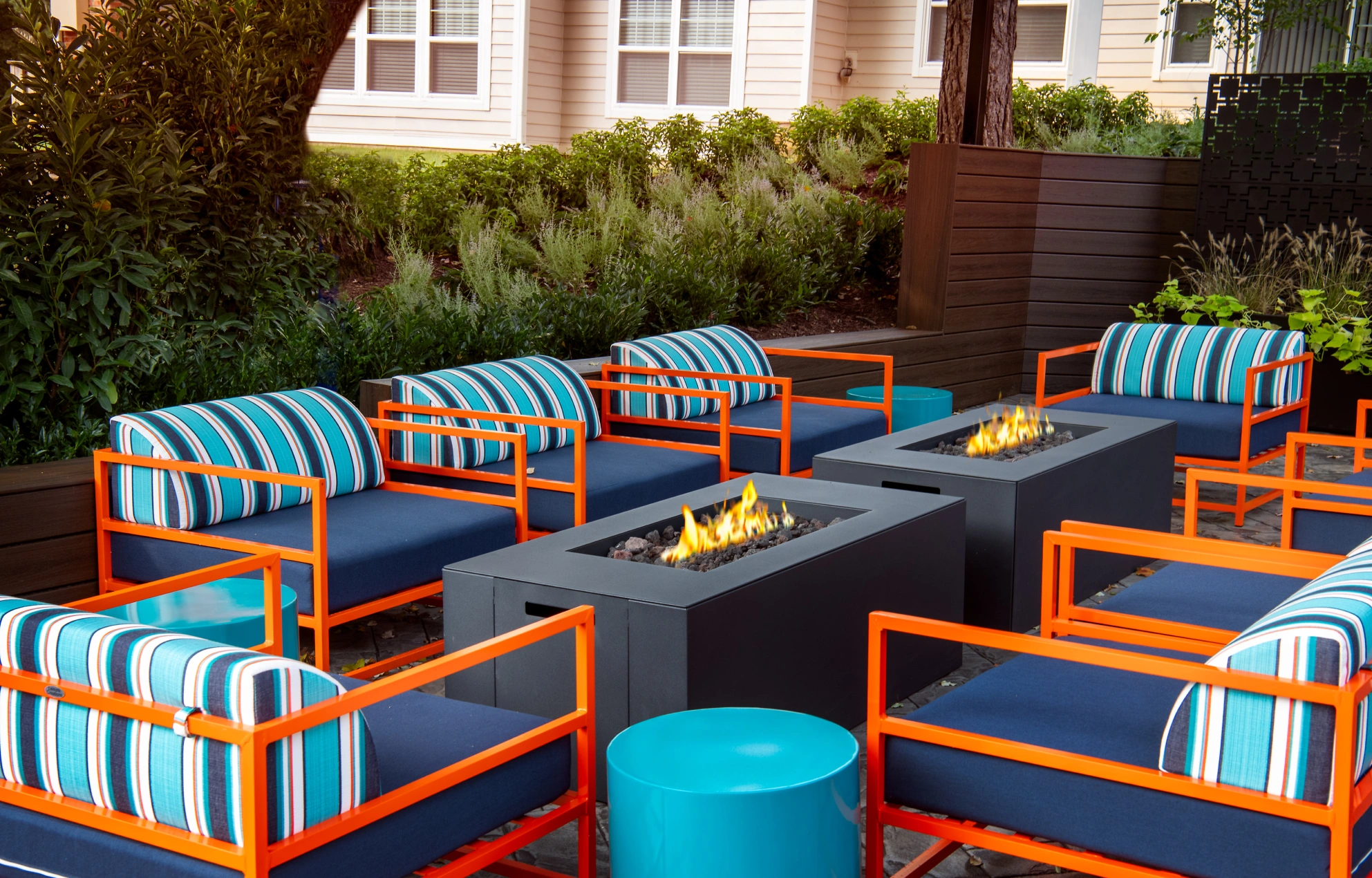 Cozy fire pit seating area with striped cushions, bold orange frames, and modern rectangular fire tables