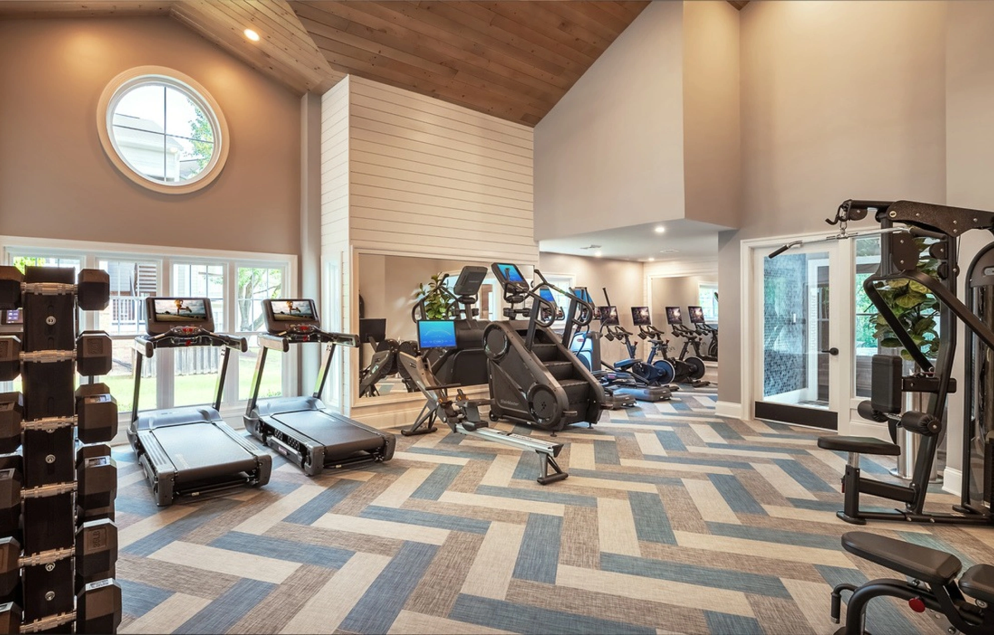 Modern fitness center with treadmills, elliptical machines, free weights, and patterned flooring