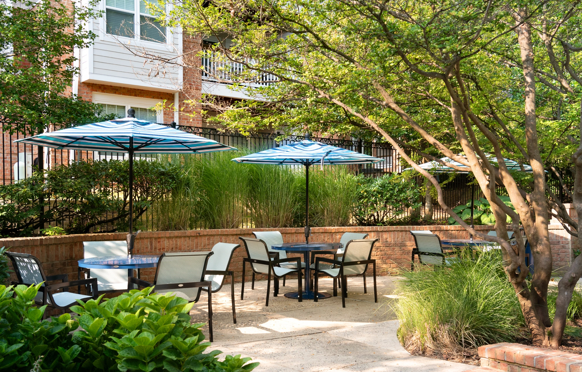 Outdoor patio seating area with striped umbrellas, garden landscaping, and multiple shaded dining tables